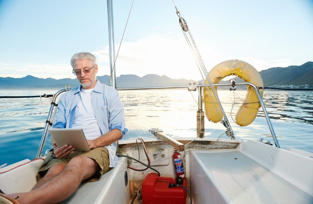 Älterer Herr sitzt entspannt mir seinem Tablett auf dem Segelschiff